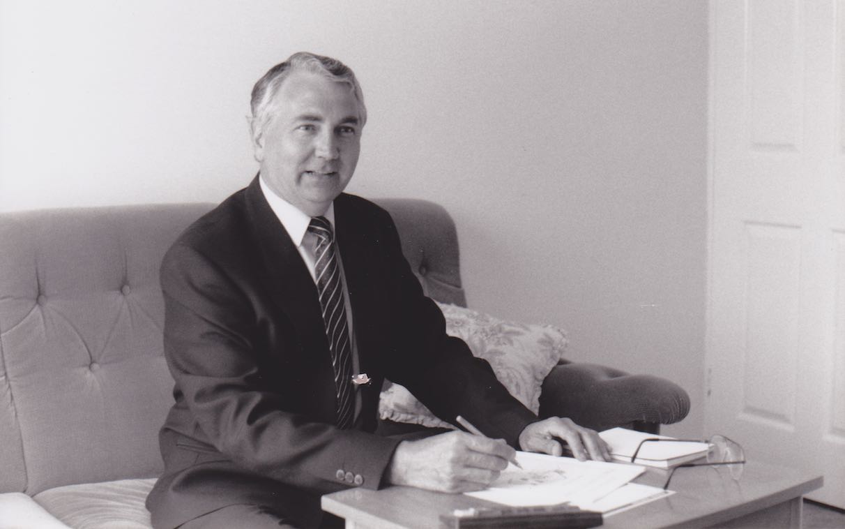 A man in a suit signing papers at a coffee table in a lounge